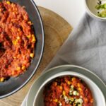 Veganes Chili sin carne serviert in einer Schüssel gemeinsam mit einer Pfanne auf dem Tisch